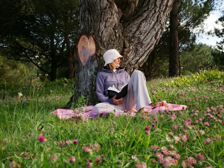 retired woman reading a book under a tree